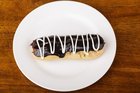A fresh eclaire on a plate with chocolate and vanilla icingの写真素材