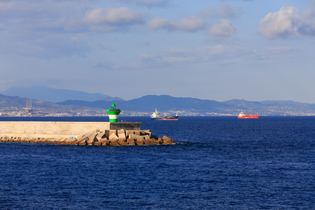 A green and white lighthouse on the end of a seawall in the harbor of Barcelonaの写真素材