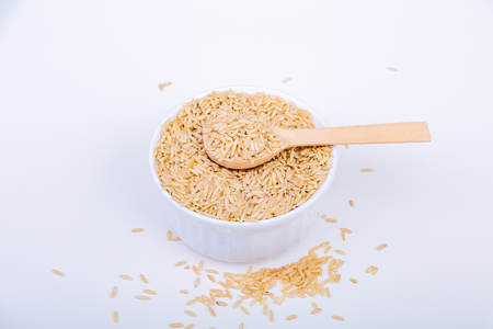 Nutritious, Whole-Grain Brown Rice in a White Bowl or Ramekin on White Background with Wood Spoonの写真素材