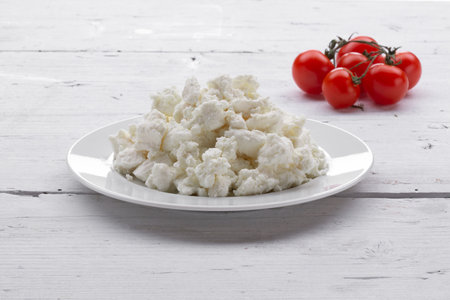 Cottage cheese in a white plate with cherry tomatoes on a white wooden backgroundの写真素材