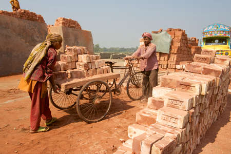 Dhaka, Bangladesh, February 19, 2014 - Two workers move bricks at a factory in Dhaka, Bangladesh. In Bangladesh women often attend very hard jobs.のeditorial素材