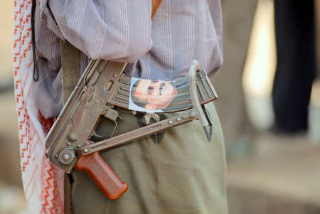 Hadramaut Valley, Yemen, September 14, 2006 - Man holds Kalashnikov machine gun, Hadramaut valley, Yemen. At the magazine - portrait of the former President of Yemen Mr. Ali Abdullah Saleh.のeditorial素材