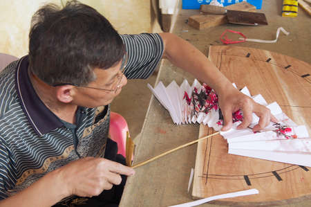 Yangshuo, China - May 04, 2009 - Man produces traditional Chinese fan in Yangshuo, China. Yangshuo town is famous in Guangxi region of China for itのeditorial素材