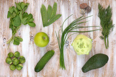 Set of green vegetables on white painted wooden background: kohlrabi, avocado, brussels sprouts, apple, cucumber, green onion, pea pods, dill, basil.の写真素材