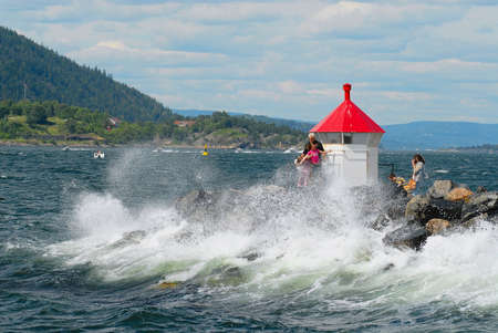 Frogn, Norway, July 08, 2006 - People make travel photos at the lighthouse with the coming wave in Frogn, Norway.のeditorial素材