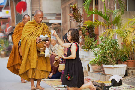 Chiang Khan, Thailand, April 18, 2010 - People offer sticky rice to Buddhist monks in the morning in Chiang Khan, Thailand.のeditorial素材