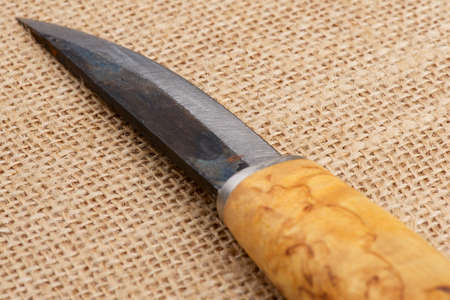 Traditional rough handmade Finnish knife with the wooden birch handle over an old sack background.