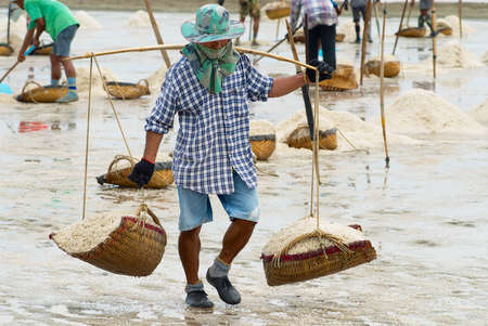 Huahin, Thailand, May 13, 2008 - Man carries salt at the salt farm in Huahin, Thailand. Salt production is one of the main industries in the Huahin area, it brings modest income to many local families.のeditorial素材