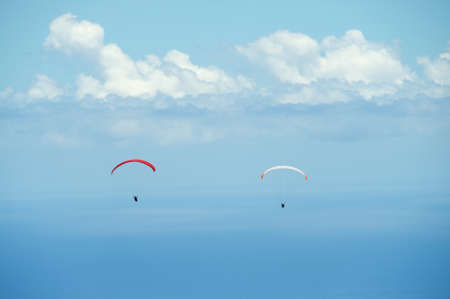 Red and white paragliders fly over Indian ocean with clouds at the background in Reunion island, France.の写真素材
