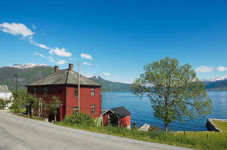 Balestrand, Norway - June 06, 2012: View to the traditional red painted Norwegian house with Sognefjord at the background in Balestrand, Norway.のeditorial素材