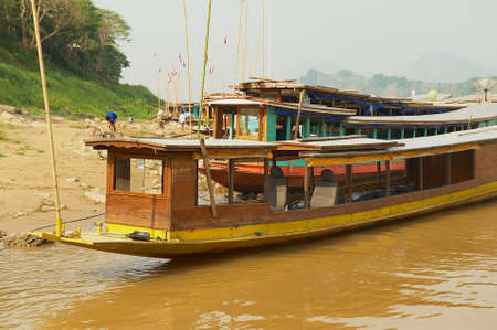 LUANG PRABANG, LAOS - APRIL 12, 2012: View to traditional long boats tied at the sandy bank of Mekong river in dry season in Luang Prabang, Laos.のeditorial素材