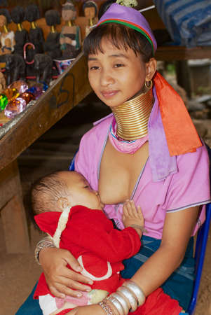 Mae Hong Son, Thailand - November 17, 2008: Young woman of the Lahwi Padaung (Long Neck) hill tribe wearing traditional decorations milk feeds her baby in Kayan village in Mae Hong Son, Thailand.のeditorial素材