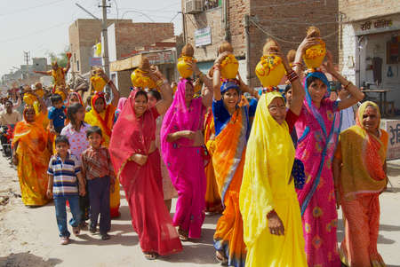 Bikaner, India, April 01, 2007: A crowd of Rajasthani women wearing yellow and red sarees holding coconuts and pots take part in a religious procession in Bikaner, India.のeditorial素材