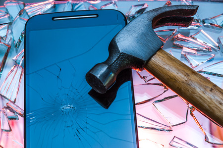 Phone with smashed screen lying on broken glass with a hammer on itの写真素材