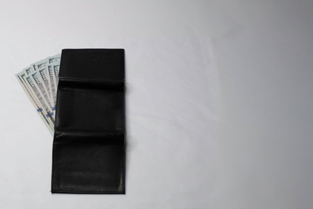 A black wallet with hundred dollar bills sticking out on a white background.