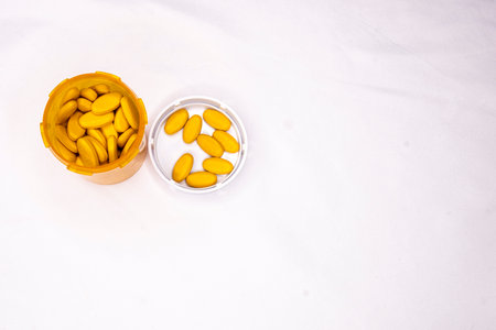 An open bottle containing orange tablets. Cap is on the table top next to the vial, contains some of the pills.の写真素材