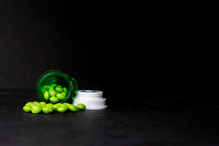 A green prescription bottle laying on its side with green 'pills' spilled out on a black background. The concept shown is that prescriptions drugs are treated like candy and misused.の写真素材