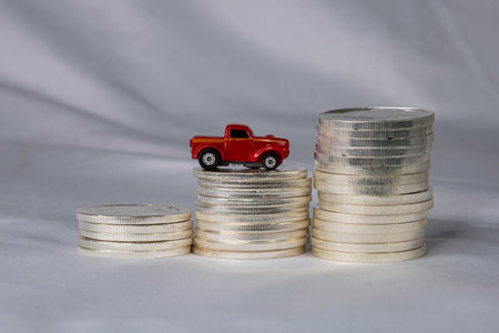 A toy truck on a coin stack of silver coins. Concept showing owernship expenses continue to increase...