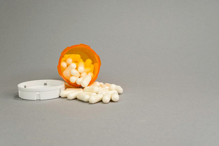 An open orange prescription bottle on its side facing front that has some capsules spilled out on a grey background.の写真素材