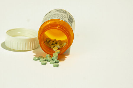 A prescription bottle laying on its side with multiple of the green blue pills spilled out in front of it. Viewed from the front.の写真素材