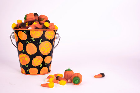 A bucket of Halloween candy overflowing onto the surface. Candy corn and pumpkins.