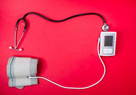 A Stethoscope and Blood Pressure monitor form a border on a red background.の写真素材