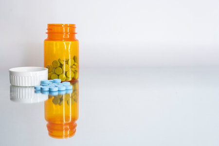 An open prescription bottle with some of its contents, blue pills, spilled out in front. Bottle and pills are on a mirror. View straight on, level view.の写真素材