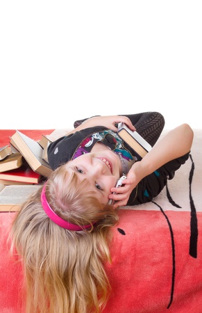 Teen girl with a book lying on the bed and talking on mobile phone isolated on whiteの写真素材