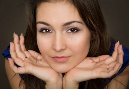 Portrait of beautiful young brunette woman propping up her face against dark background.の写真素材