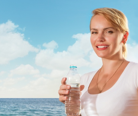 Beautiful woman smiling with water bottle in hand on tropical beachの写真素材