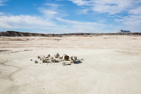 A desert scene with a large flat area of dirt and a broken boulder in a pile in the foreground. In the background are small brown hills and a large plateau in the distance.の写真素材