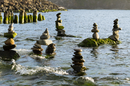 Six cairns all with unique shapes are perched on larger rocks  overlooking the ocean as the tide rises to overtake themの写真素材