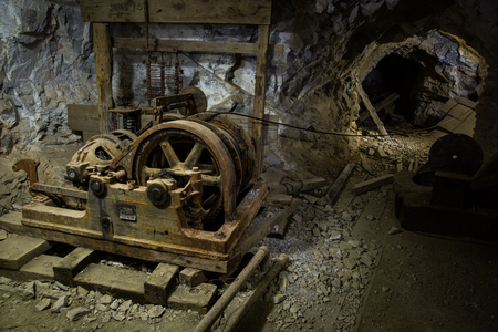 An old hoist and several other pieces of worn-down mining equipment inside of an abandonned mine in Western Utah. The hoist would have been used to pull loaded mine carts up a nearby steep sloping shaft before they were pushed out of the mine to process tのeditorial素材