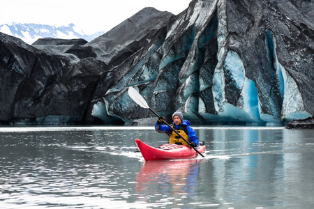 A man paddles his kayak away from the terminus of the Spencer Glacier. The ice is covered with dark moraine - dirt and rock ground up by the glacier.の写真素材