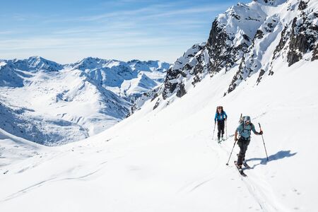 Two skiers skinning uphill on a hot sunny day in the Alaska backcountry of the Talkeetna Mountains.