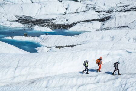 Three ice climbing and glacier trekking guides hiking across the white ice of the Matanuska Glacier.の写真素材