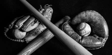 Dark black and white image of old baseball gear that has been well loved. Scratched, scuffed and peeling from years of play.の写真素材
