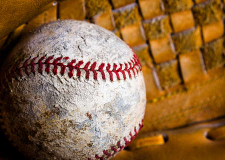 Closeup of baseball in a mitt. The ball is old and damaged, well used with scuffs, stains, and stitching out in places.の写真素材