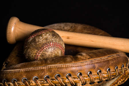 Old baseball, stained and wonrn out, and old style catchers mitt joined by a brand new baseball bat.