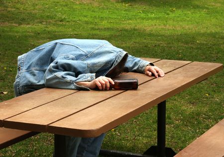 man assleep on a picinic table with beer bottle in handの写真素材