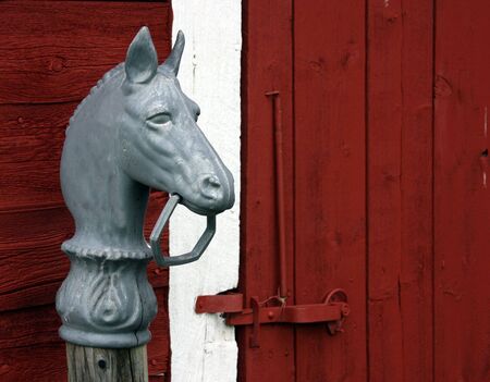 horse hitching post in front of a red barn latched doorの写真素材