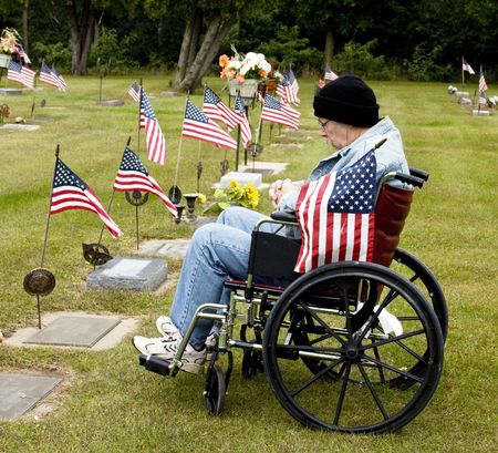 disabled war vet in a wheelchair holding american flag at a grave siteの写真素材