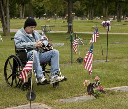 disabled american veteran at a grave holding an American flagの写真素材