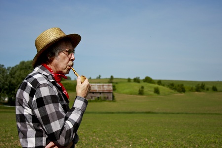 farmer in straw hat with a corn cob pipe standing on a green fieldの写真素材