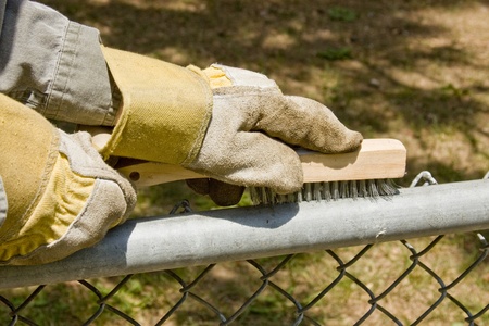 worker with gloves on wire brushing a chain link fenceの写真素材