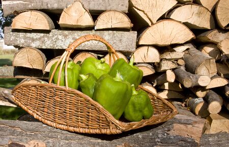 green peppers in a wicker basket with a wood pile backgroundの写真素材