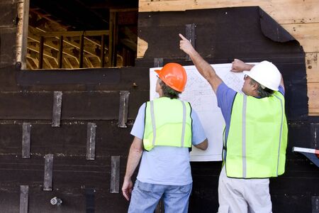two architect contractors looking at blueprints against a building being built