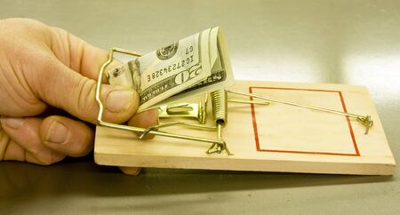 persons hand caught in a mouse trap taking a twenty dollar bill