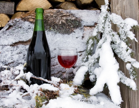 bottle and glass of wine chilled by snow on a wood pile of firewoodの写真素材