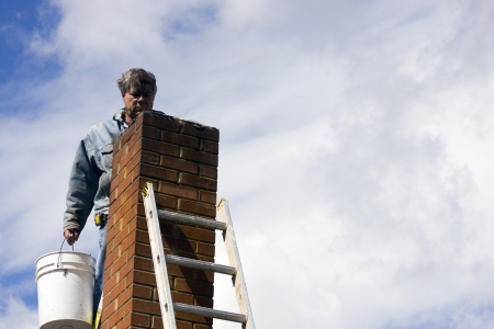 brick mason on a ladder repairing damaged chimneyの写真素材